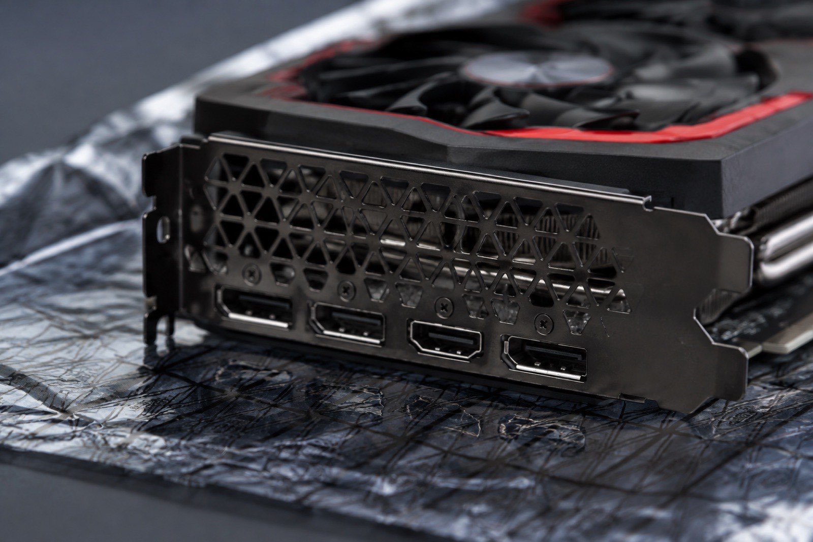 Illustration: the rear bracket and display outputs of a red-accented graphics card resting on an anti-static bag